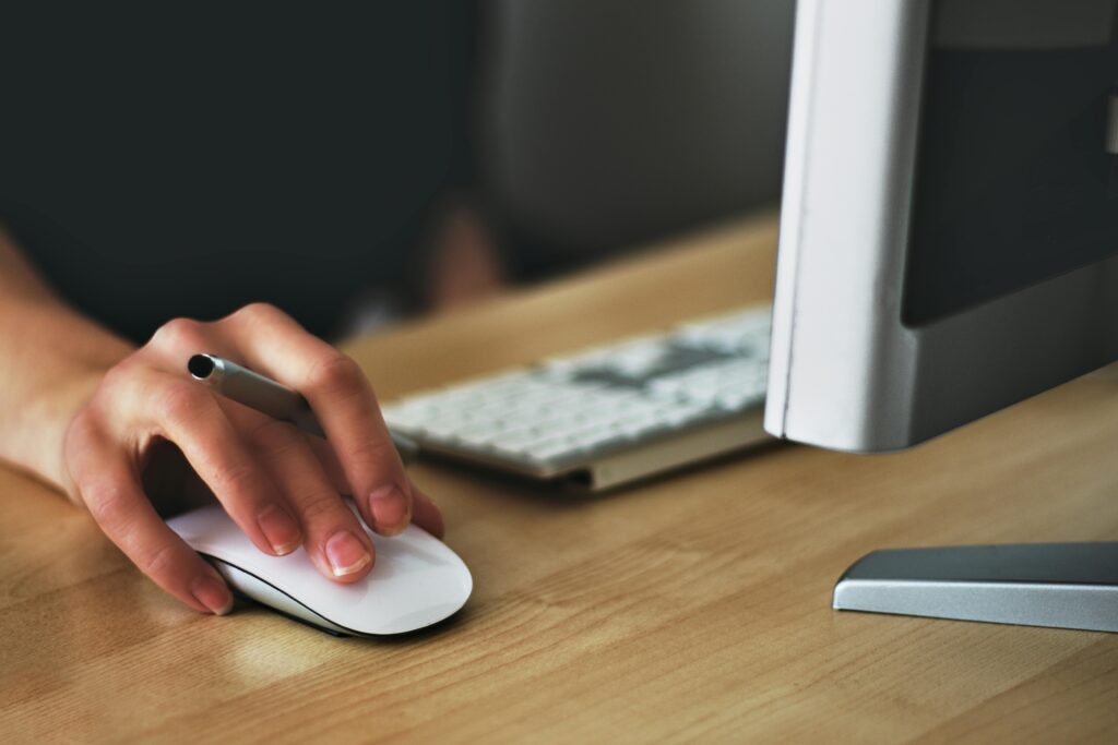 Hand holding an Apple Magic Mouse beside a keyboard, symbolizing precise digital workflows and clean, validated product data managed through a PIM system.